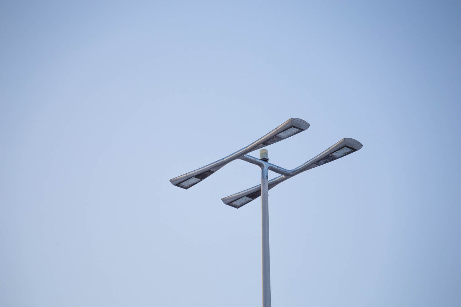 A modern streetlight with two double-headed lamps against a clear blue sky.
